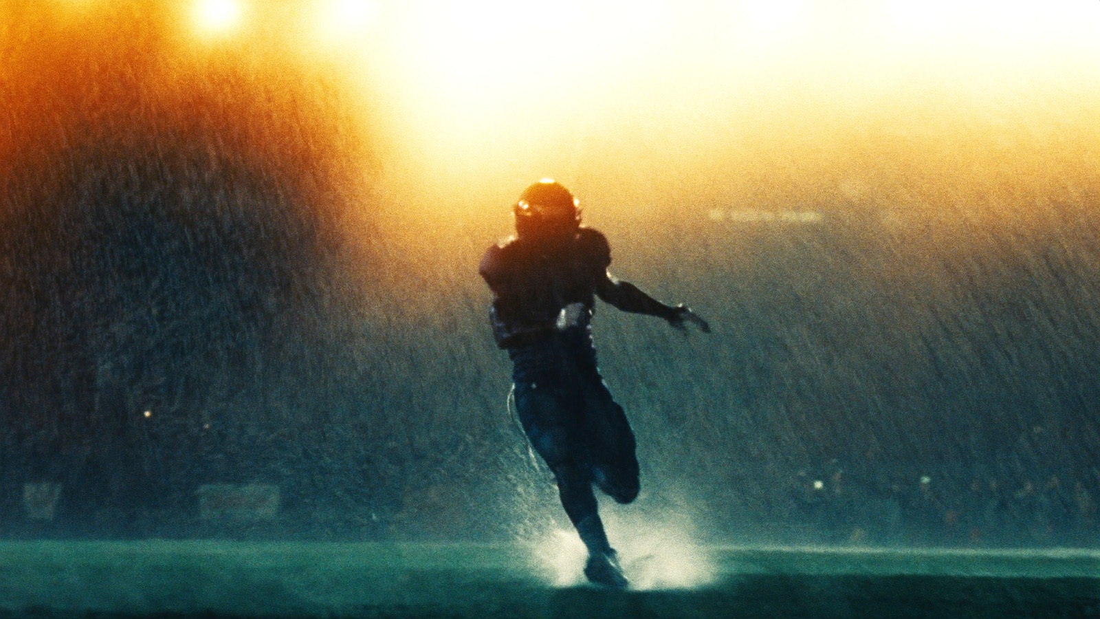 A lone football player silhouetted against stadium floodlights in heavy rain.