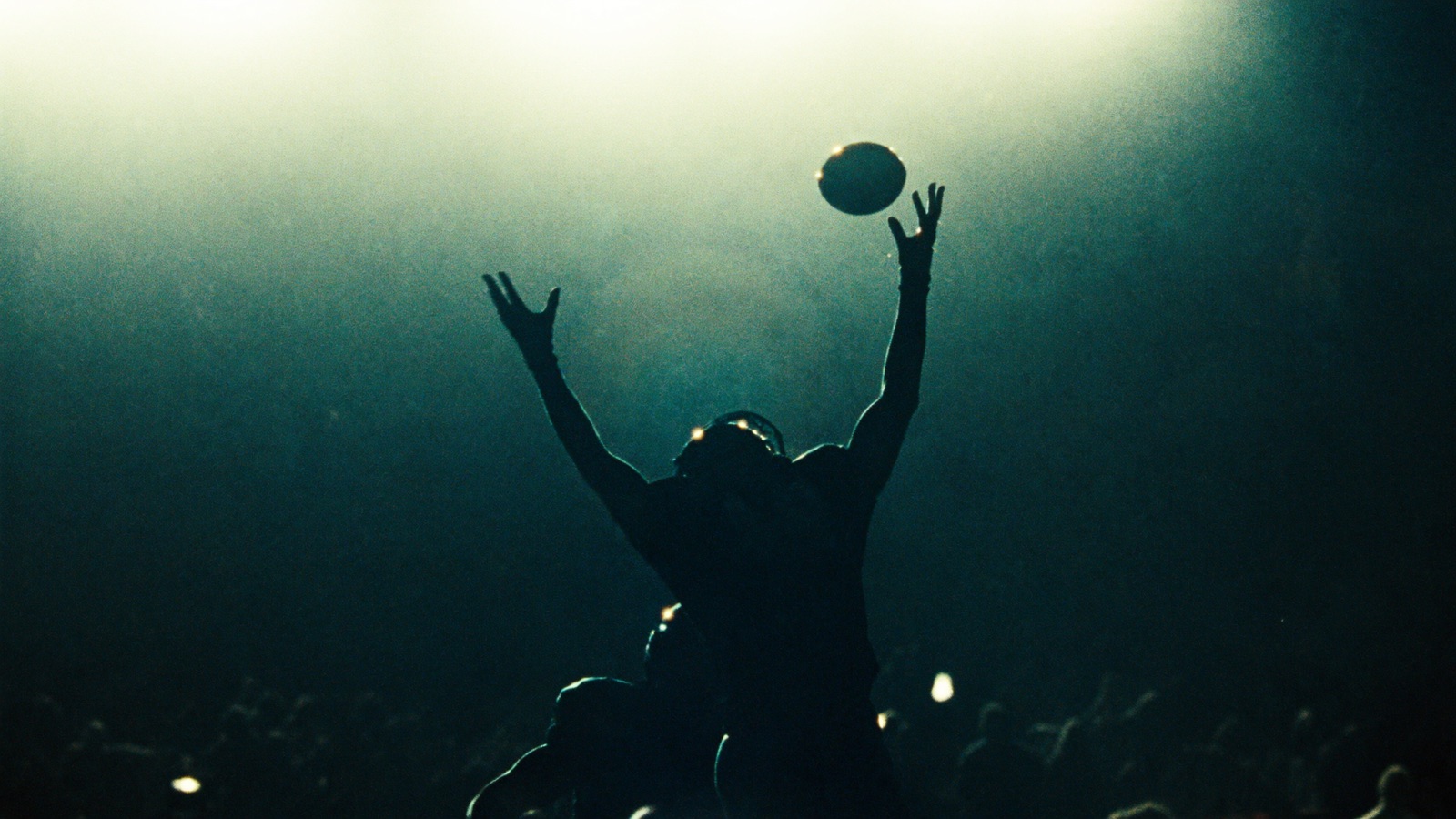 A receiver silhouetted mid-air against stadium floodlights, reaching for a deep ball.